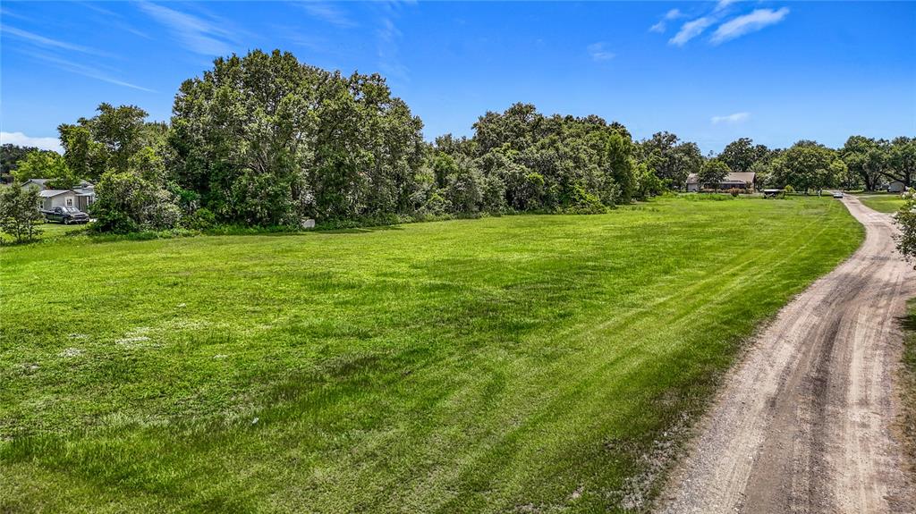 A large, grassy vacant lot borders a dirt road with trees in the background — 7211 TUMBLETON CT, DOVER, FL