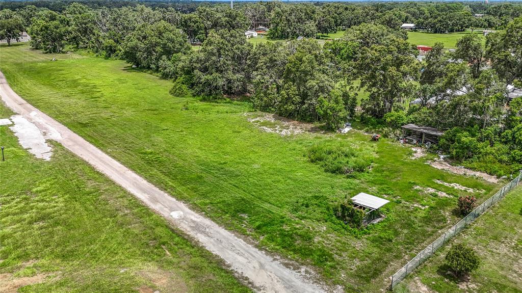 An aerial view shows a grassy, undeveloped lot bordered by a dirt road and trees — 7211 TUMBLETON CT, DOVER, FL