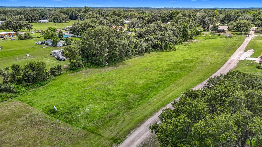 An aerial view shows a large, grassy vacant lot bordering a dirt road and trees — 7211 TUMBLETON CT, DOVER, FL