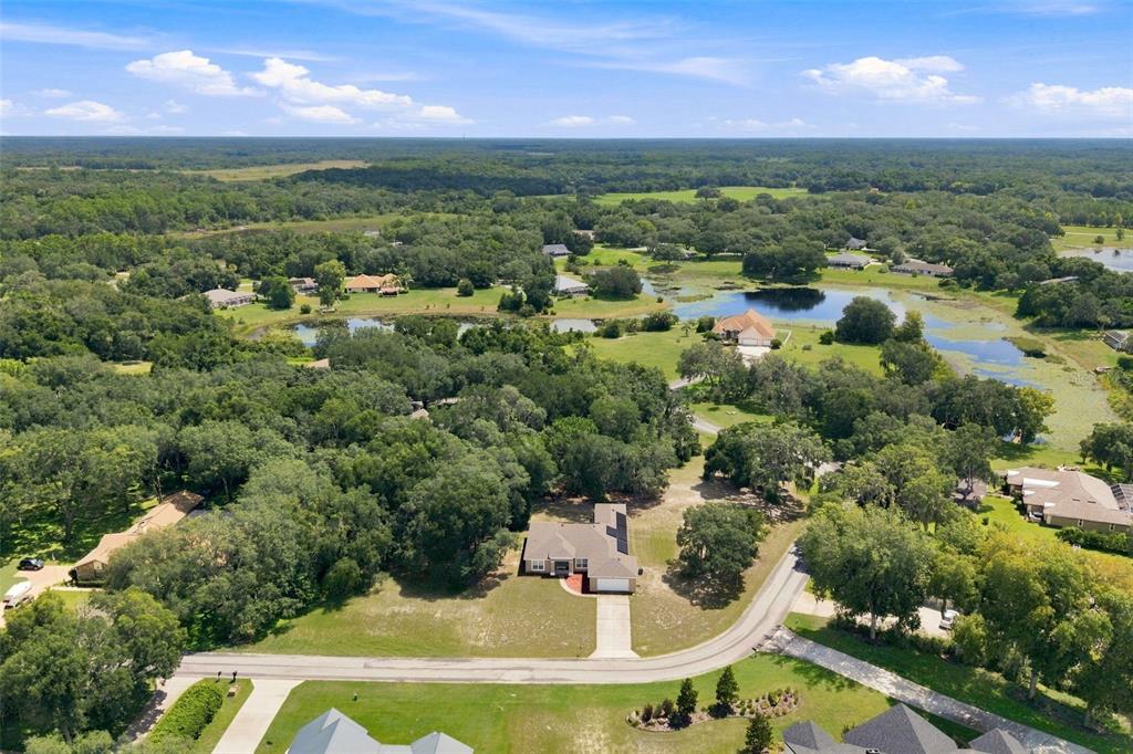 An aerial view shows a single-story house surrounded by trees, lawns, and nearby ponds — 9495 E BAYMEADOWS DRIVE, INVERNESS, FL