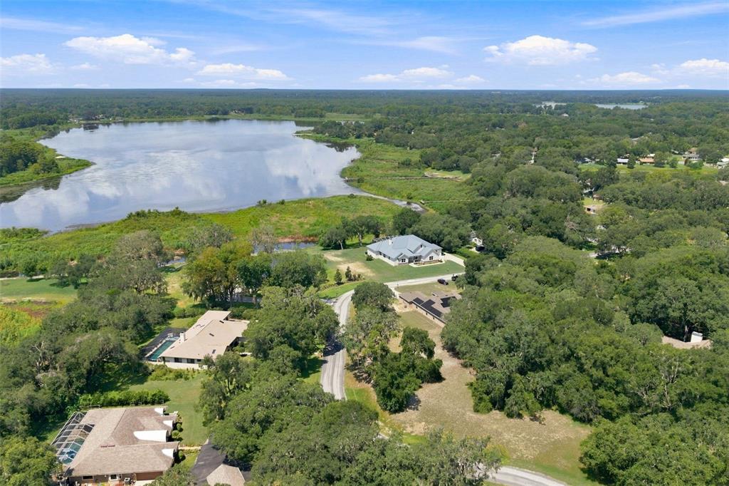 An aerial view shows several houses surrounded by dense trees near a large lake — 9495 E BAYMEADOWS DRIVE, INVERNESS, FL