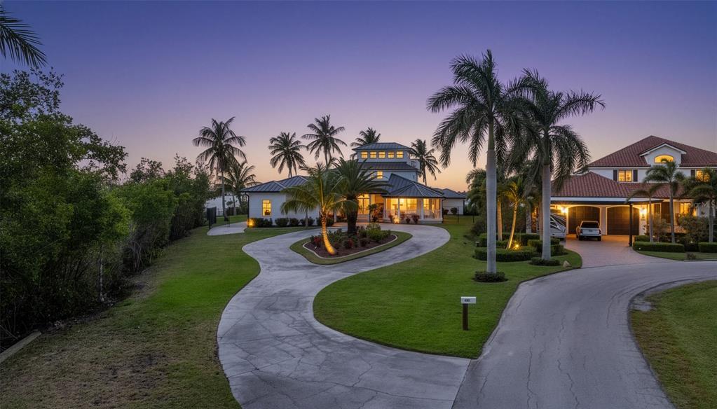 A large house with a circular driveway, palm trees, and a manicured lawn at dusk — 12201 SHOREVIEW DRIVE, MATLACHA, FL