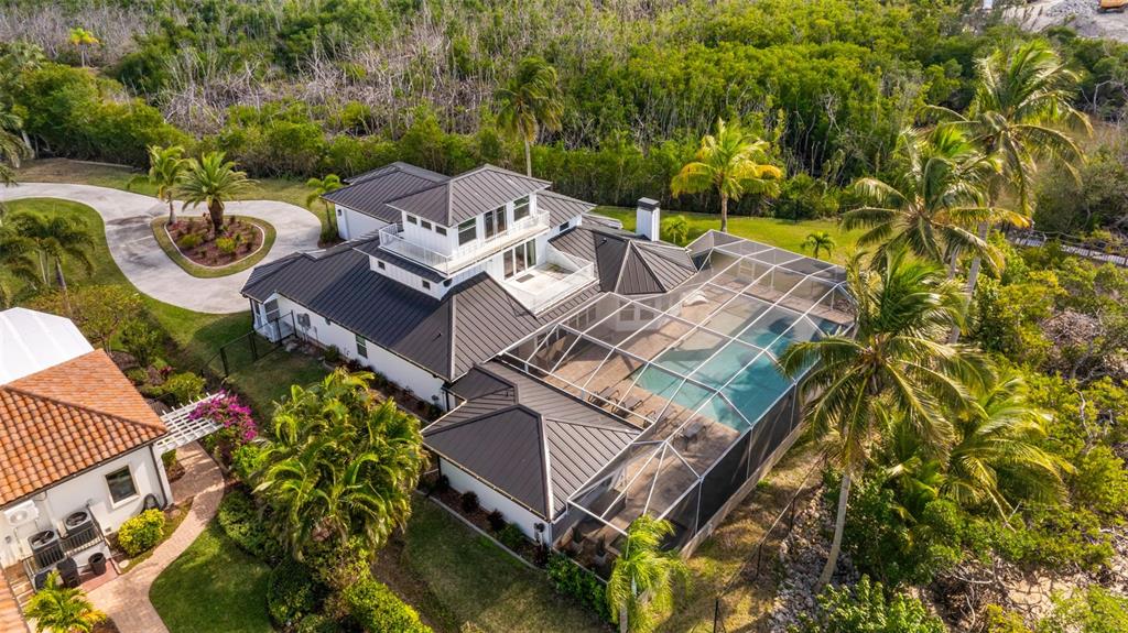 An aerial view shows a white house with a dark metal roof and screened pool — 12201 SHOREVIEW DRIVE, MATLACHA, FL