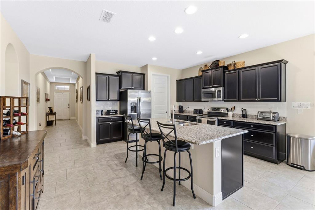 A kitchen features dark cabinets, granite countertops, a center island with stools, and tile flooring — 8711 EDEN COVE DRIVE, WINTER GARDEN, FL