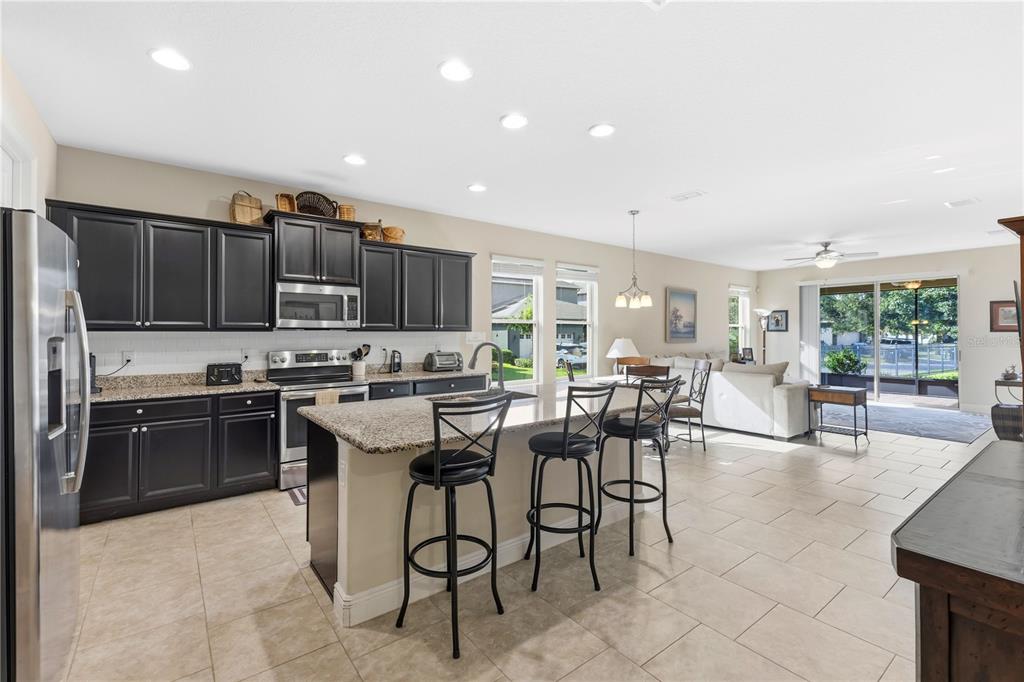 A kitchen with dark cabinets and granite countertops opens to a living area with tile floors — 8711 EDEN COVE DRIVE, WINTER GARDEN, FL