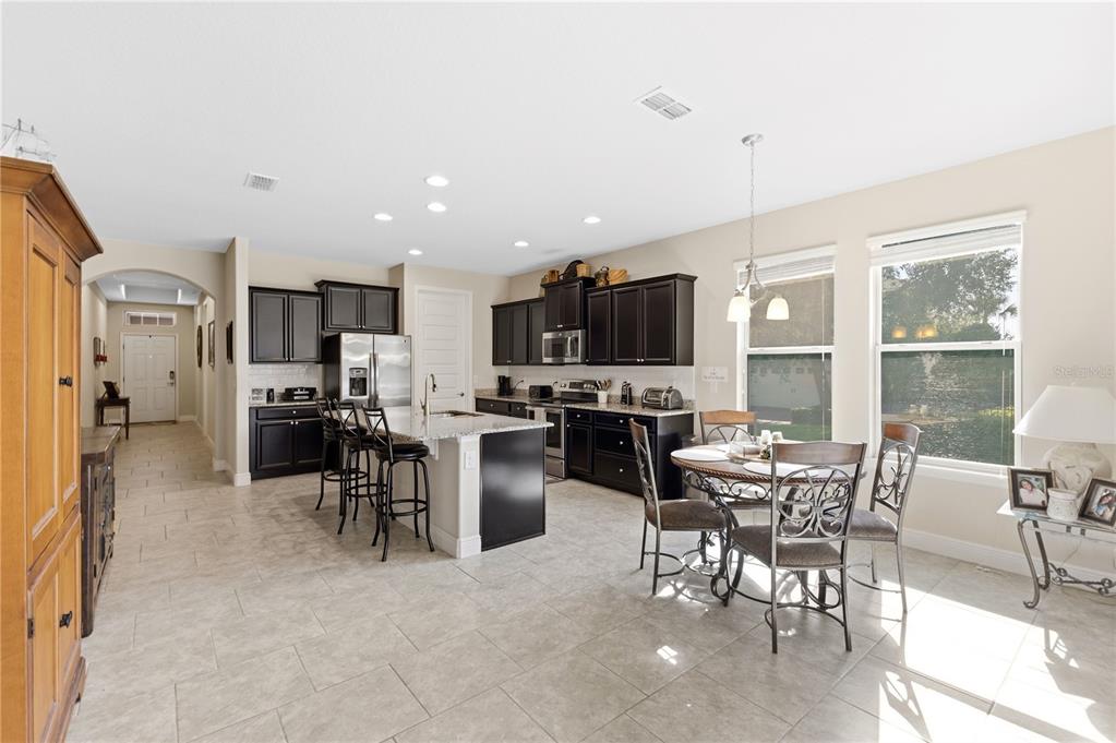 A kitchen with dark cabinets, granite countertops, a center island, and an adjacent dining area — 8711 EDEN COVE DRIVE, WINTER GARDEN, FL
