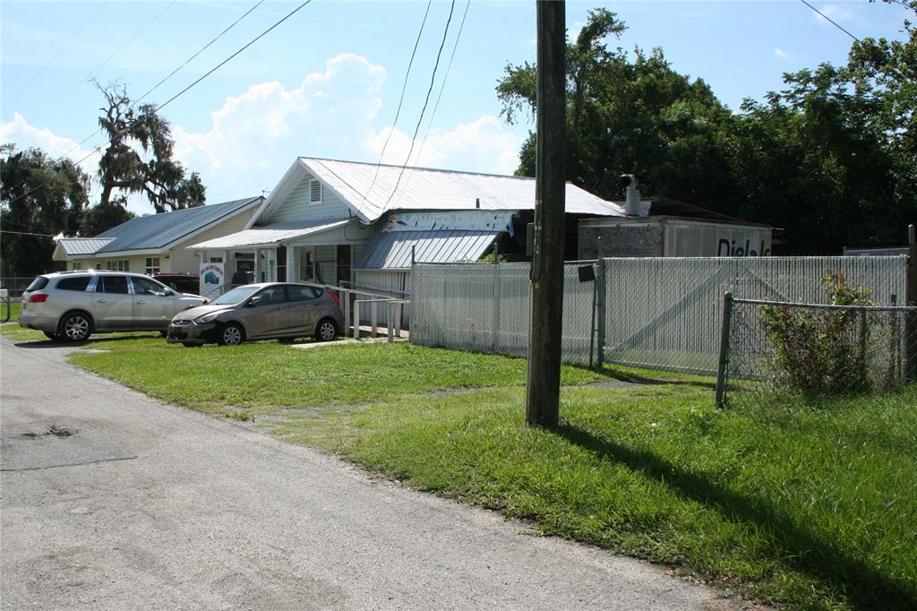 A light-colored house with a metal roof sits behind a chain-link fence near parked cars — 236 NE 13TH PLACE, OCALA, FL