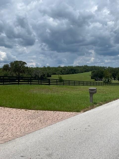 A paved road leads past a black fence bordering a large, grassy pasture with trees — 5610 EAST ORION CT, FLORAL CITY, FL