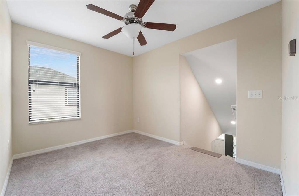 A carpeted room with a ceiling fan, a window, and an open staircase — 11714 LAKE BOULEVARD, NEW PORT RICHEY, FL