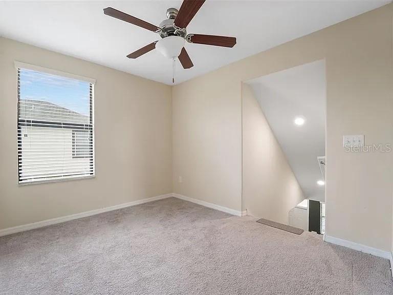 An empty carpeted room features a ceiling fan and an open staircase leading downward — 11714 LAKE BOULEVARD, NEW PORT RICHEY, FL
