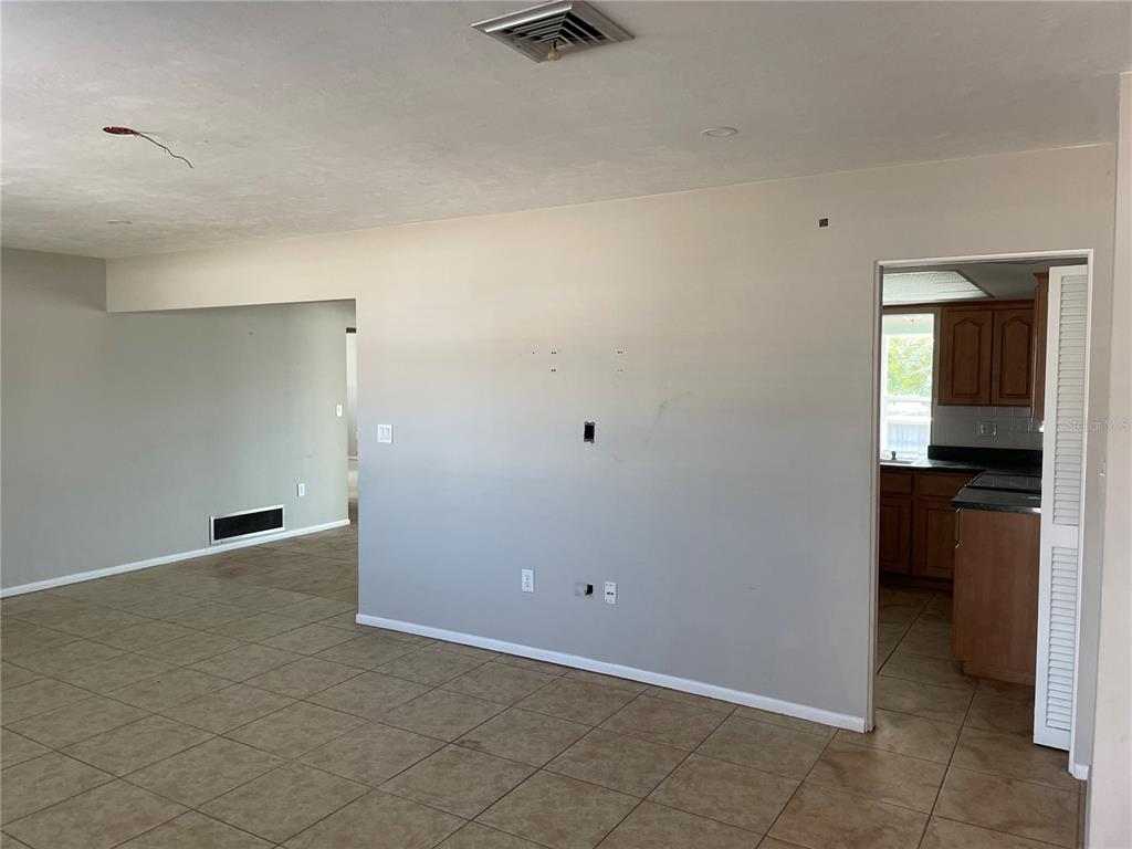 A living room with beige tile flooring, light gray walls, and a doorway to a kitchen — 10307 SANDPIPER ROAD W, BRADENTON, FL