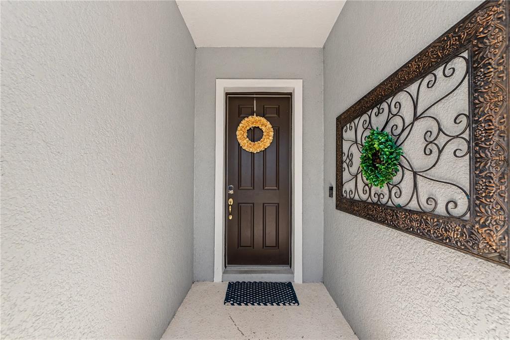 A brown front door with a wreath sits in a covered entryway with gray walls — 4213 PINE MEADOW DRIVE, PARRISH, FL