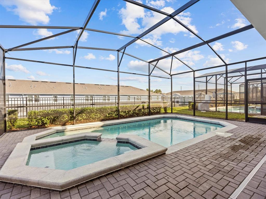 A screened-in patio features a swimming pool, a built-in spa, and brick paver decking — 3281 LILAC WAY, DAVENPORT, FL