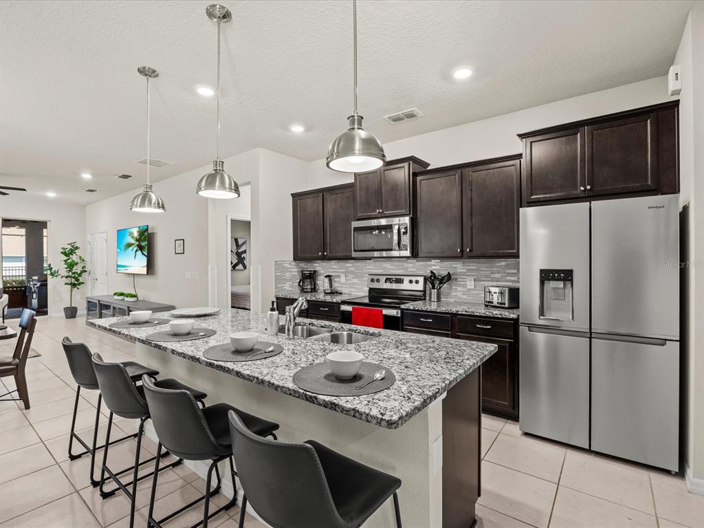 A kitchen features dark wood cabinets, granite countertops, stainless steel appliances, and a breakfast bar — 3281 LILAC WAY, DAVENPORT, FL