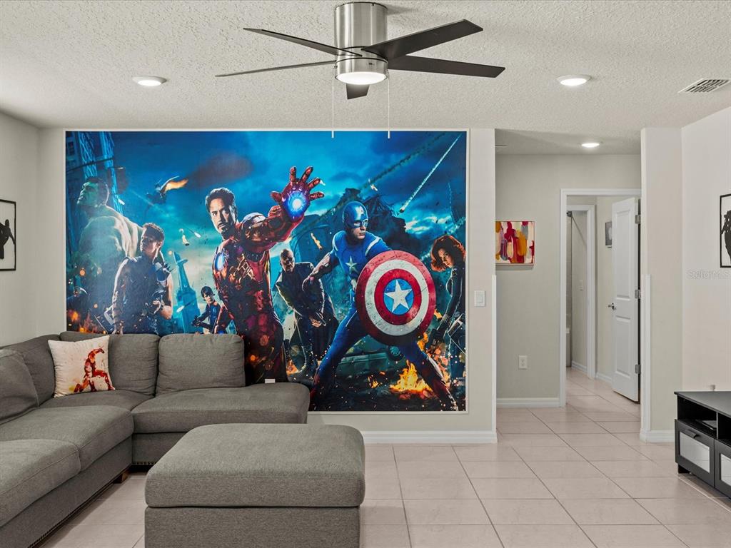 A living room features a large Avengers wall mural, a gray sectional sofa, and a ceiling fan — 3281 LILAC WAY, DAVENPORT, FL