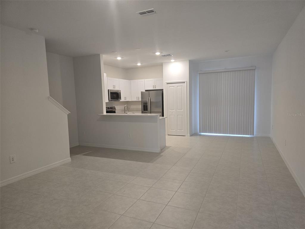 An open-concept kitchen with white cabinets and stainless steel appliances overlooks a tiled living area — 9343 CANNON BEACH DRIVE, PARRISH, FL