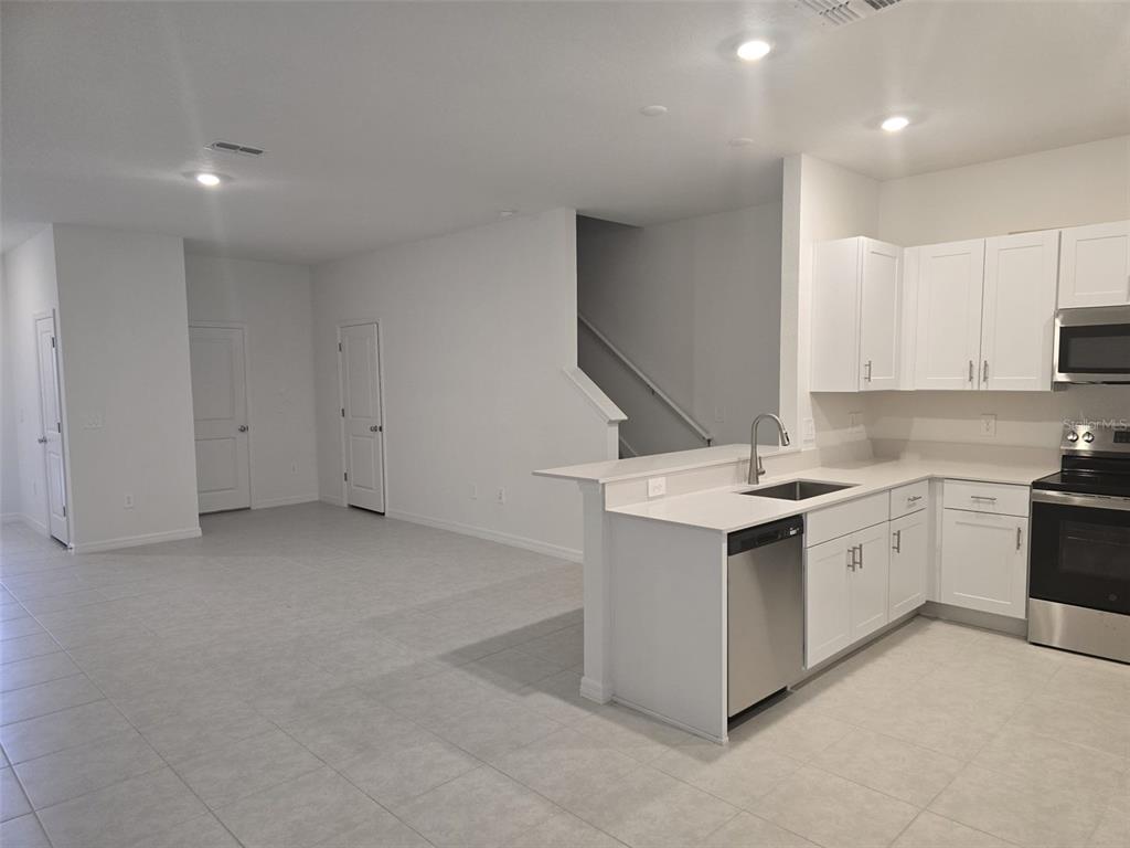 A kitchen with white cabinets and stainless steel appliances opens to a tiled living area — 9343 CANNON BEACH DRIVE, PARRISH, FL