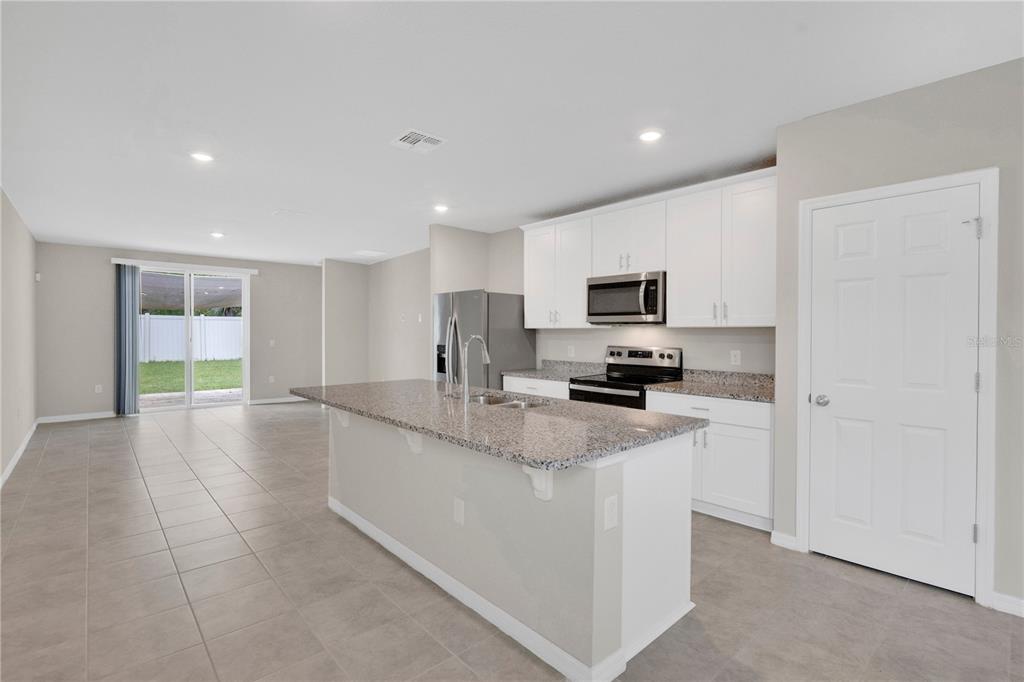 A kitchen with white cabinets, granite countertops, and a center island opens to a living area — 17403 MILLION LAKES COURT, CLERMONT, FL