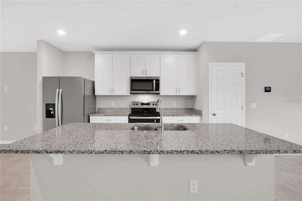 A kitchen features a granite-topped island, white cabinets, stainless steel appliances, and light gray walls — 17403 MILLION LAKES COURT, CLERMONT, FL