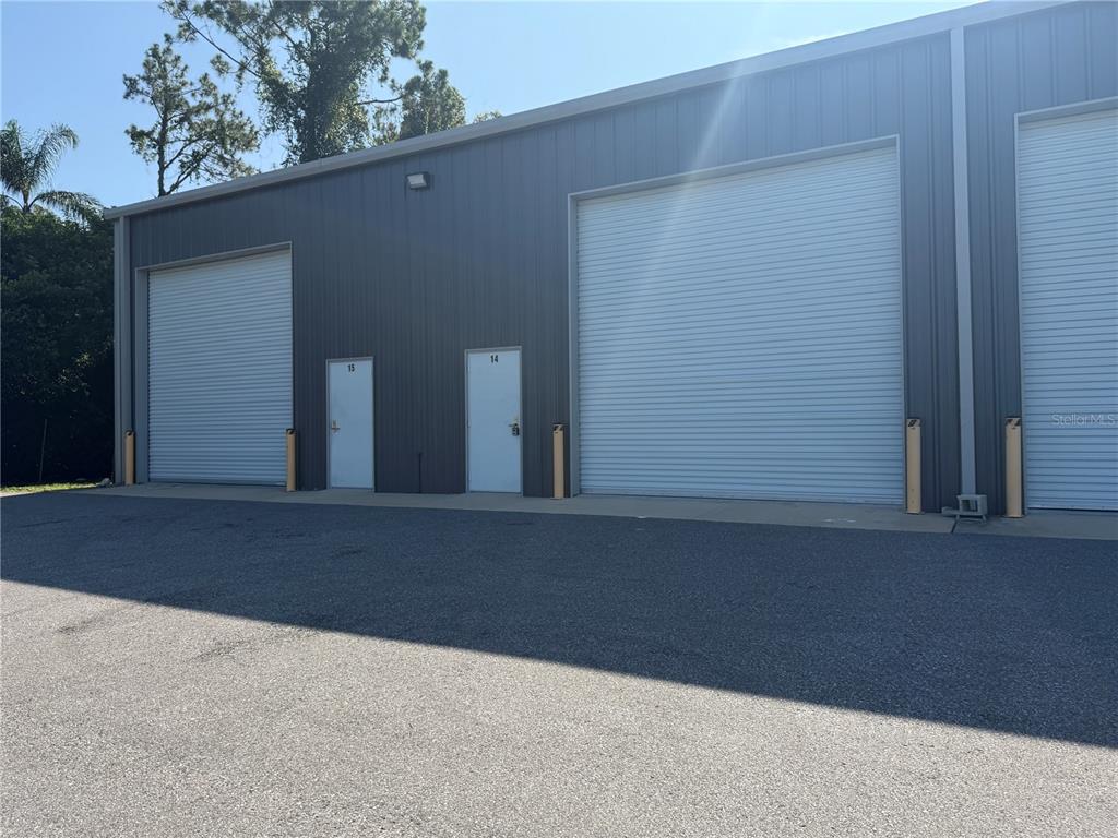 The exterior of a gray metal industrial building features two roll-up doors and two entry doors — 5475 DOVE DRIVE UNIT 14, NEW PORT RICHEY, FL