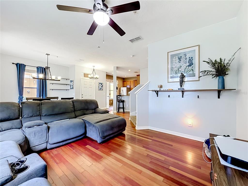A living room with hardwood floors, a gray sectional sofa, and a wall-mounted shelf — 3531 PINE OAK TRAIL, SANFORD, FL