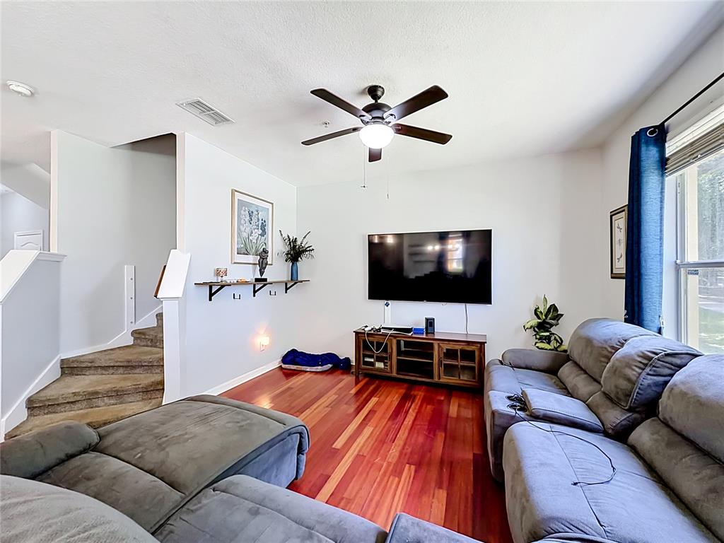 A living room features hardwood floors, a ceiling fan, a wall-mounted television, and a staircase — 3531 PINE OAK TRAIL, SANFORD, FL