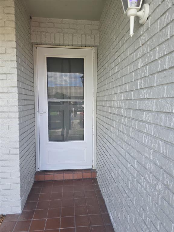 A white storm door is set into a light-colored brick wall above a tiled porch — 2912 WAINWRIGHT COURT, NEW PORT RICHEY, FL