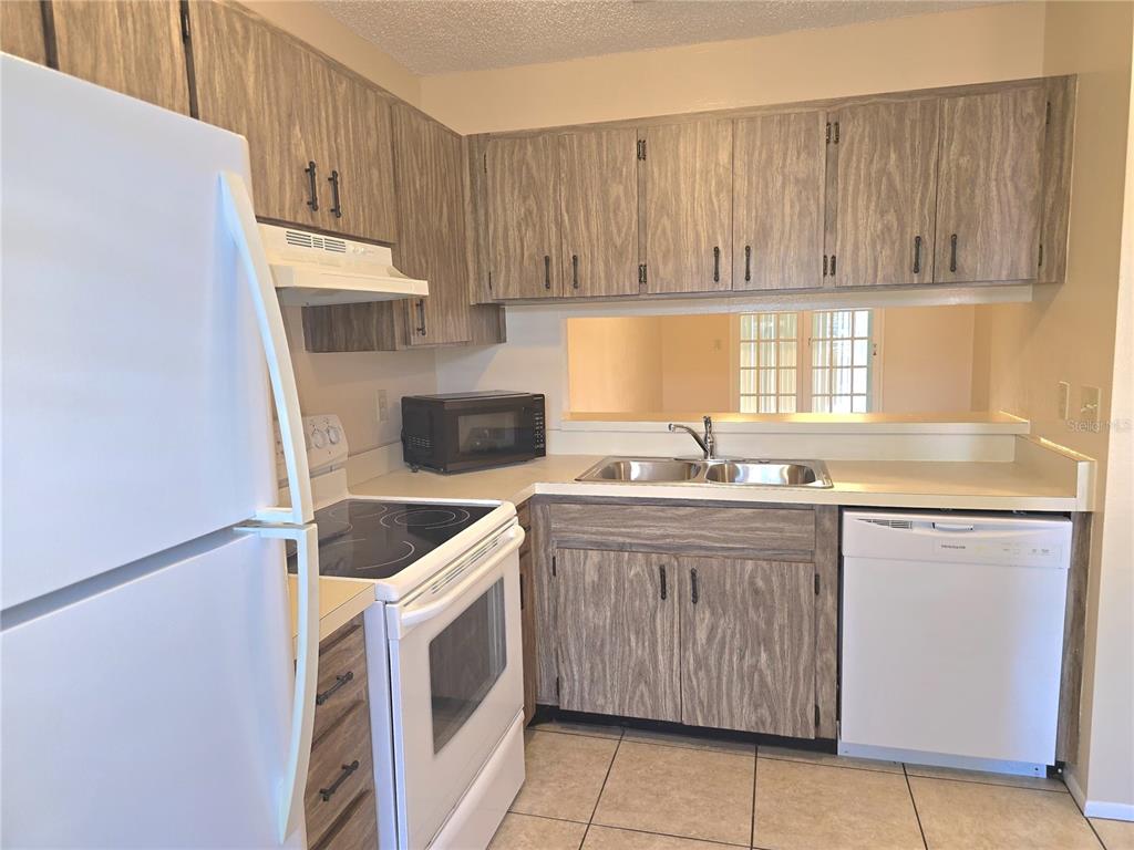 A kitchen features wood-grain cabinets, white appliances, a double sink, and light-colored tile flooring — 2912 WAINWRIGHT COURT, NEW PORT RICHEY, FL