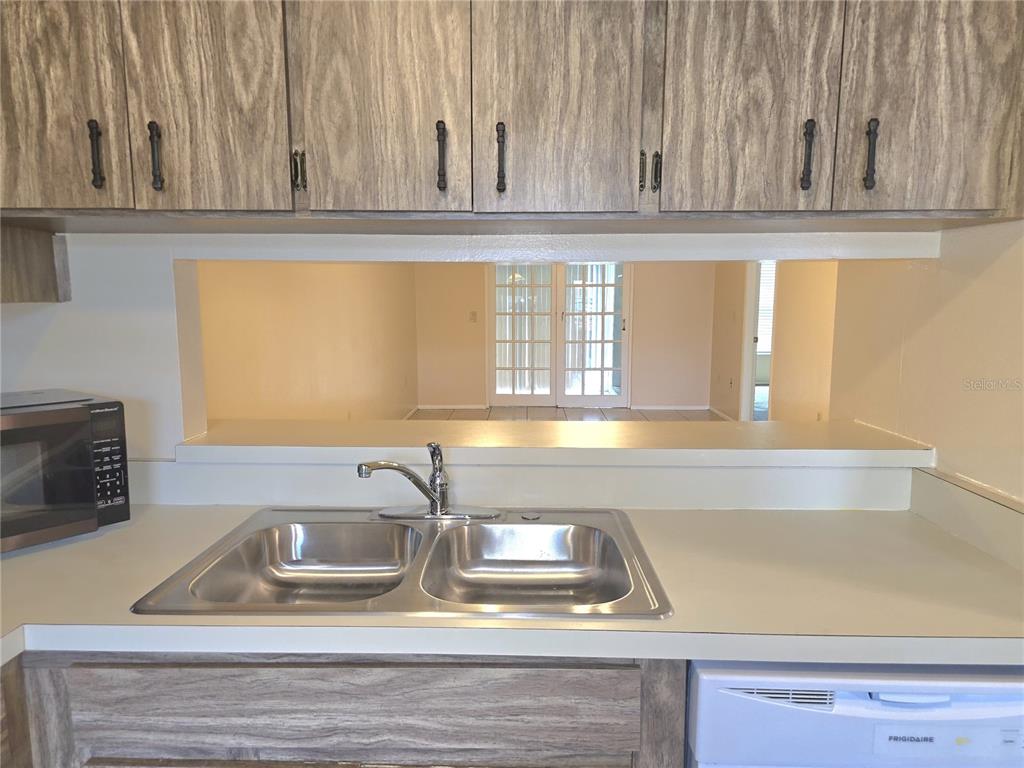 A kitchen sink and countertop are positioned below wooden cabinets with a view into another room — 2912 WAINWRIGHT COURT, NEW PORT RICHEY, FL