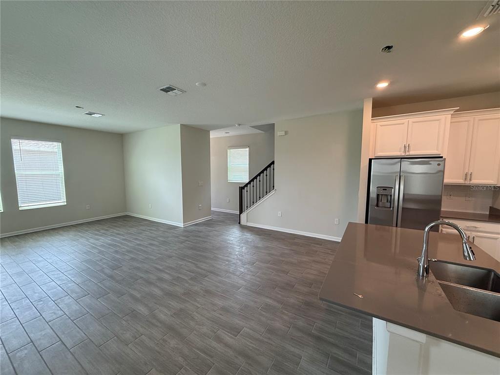 An open-concept kitchen and living area features gray wood-look tile flooring and white cabinetry — 17016 QUICKSILVER AVENUE, WINTER GARDEN, FL