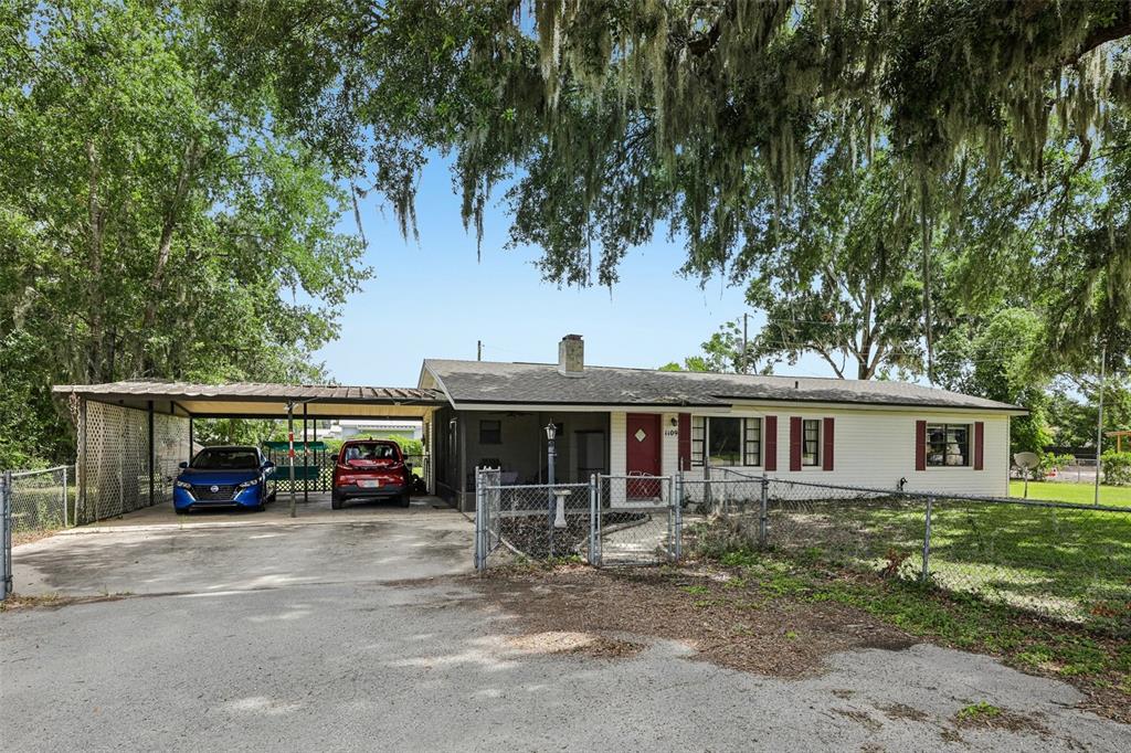 A single-story house with a carport, red front door, and a chain-link fenced yard — 1109 W C 48, BUSHNELL, FL