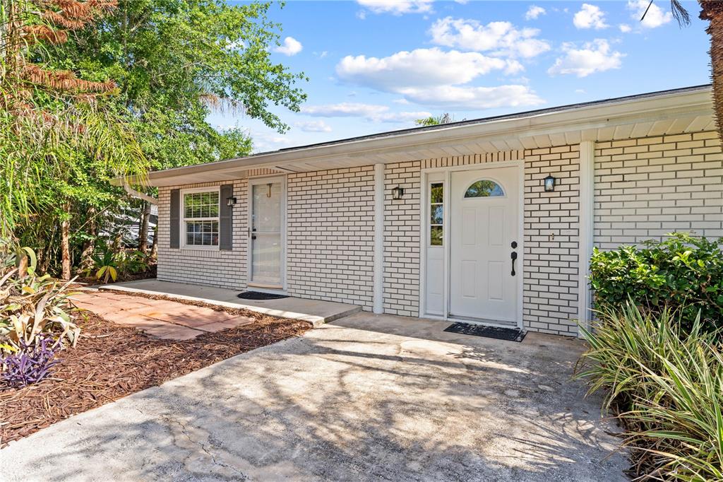 A white brick house exterior features two entry doors, a window, and a concrete driveway — 1770 PLEASANT HILL ROAD, KISSIMMEE, FL
