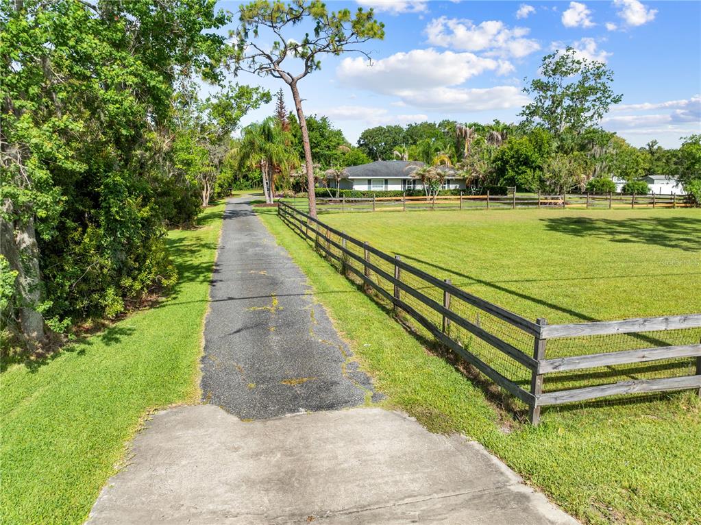 A long paved driveway leads to a single-story house bordered by a wooden fence — 1770 PLEASANT HILL ROAD, KISSIMMEE, FL