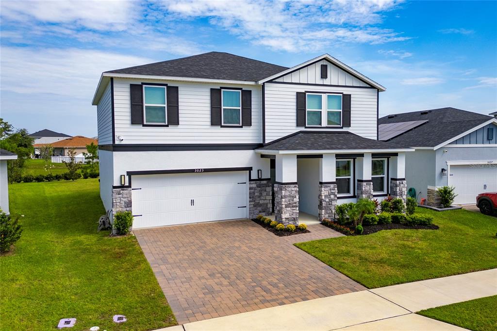 A two-story house with white siding, stone accents, a two-car garage, and a paved driveway — 3023 SANCTUARY DRIVE, CLERMONT, FL