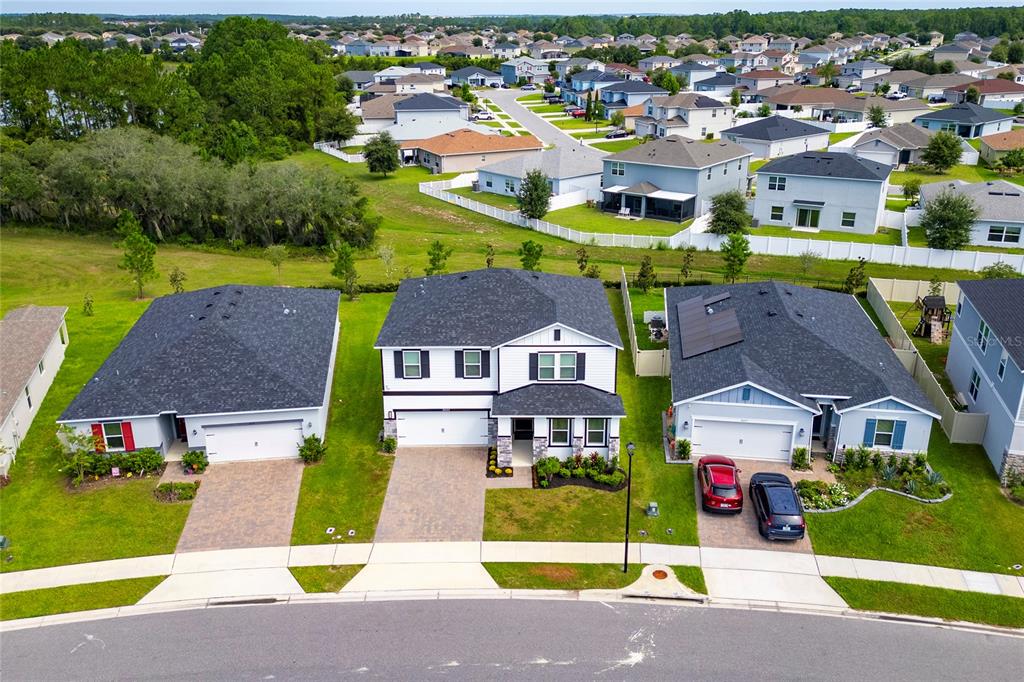 An aerial view shows three suburban houses with driveways and lawns along a curved street — 3023 SANCTUARY DRIVE, CLERMONT, FL