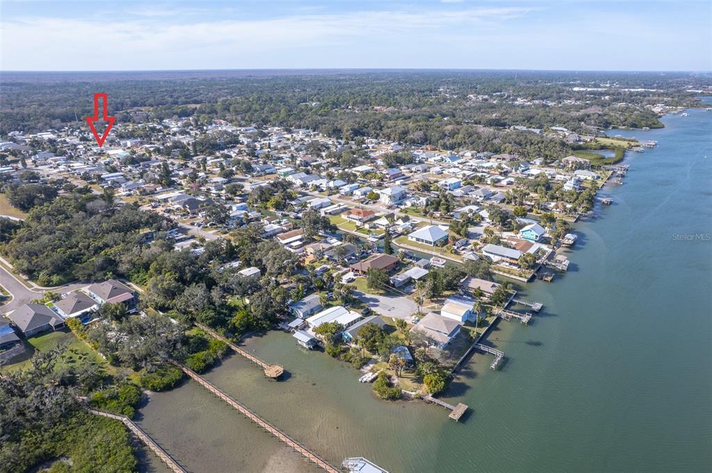 An aerial view shows a coastal neighborhood with houses, trees, and a long wooden pier — 116 LEWIS STREET, EDGEWATER, FL