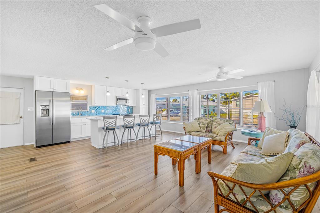 An open-concept living room and kitchen with wood-look flooring, white cabinets, and wicker furniture — 116 LEWIS STREET, EDGEWATER, FL