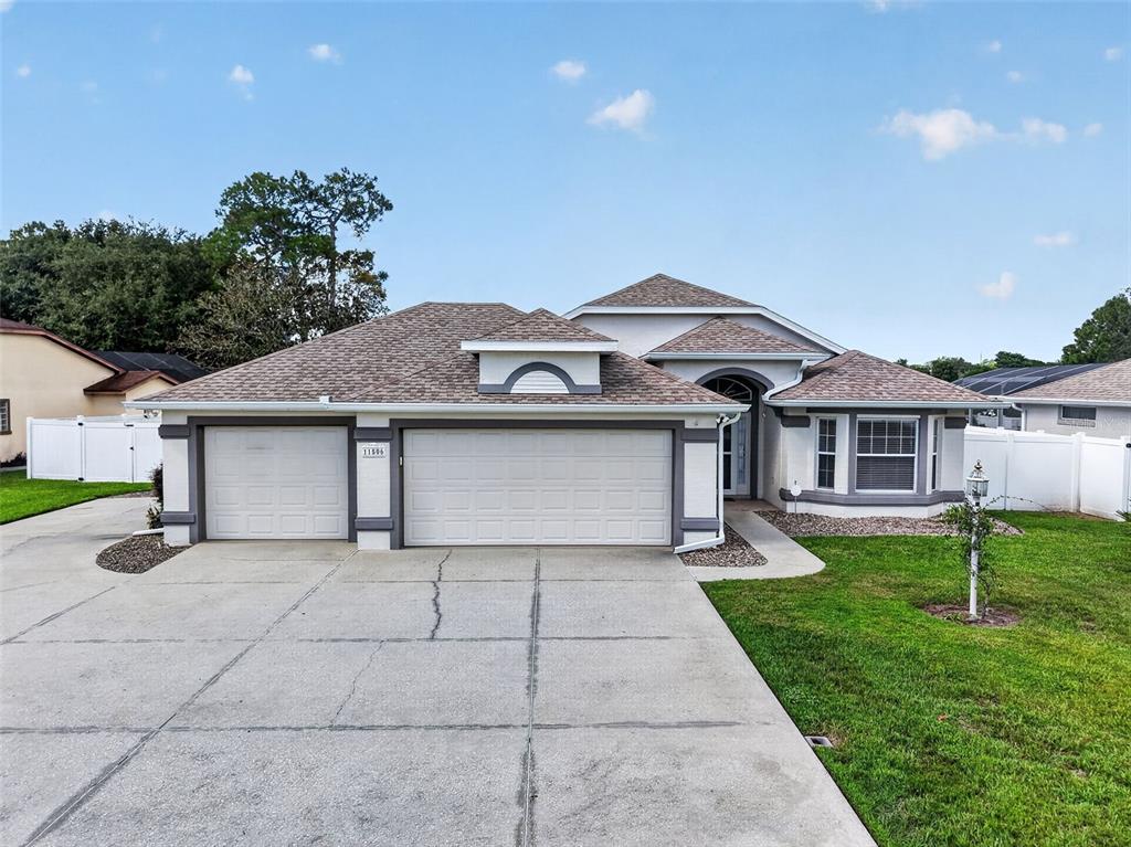 A single-story suburban house features a three-car garage, a concrete driveway, and a white fence — 11506 LAKE DR, LEESBURG, FL
