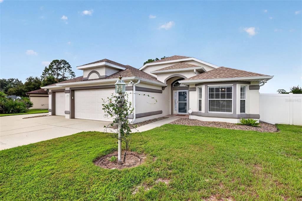 A single-story house with a two-car garage, beige stucco exterior, and a shingled roof — 11506 LAKE DR, LEESBURG, FL