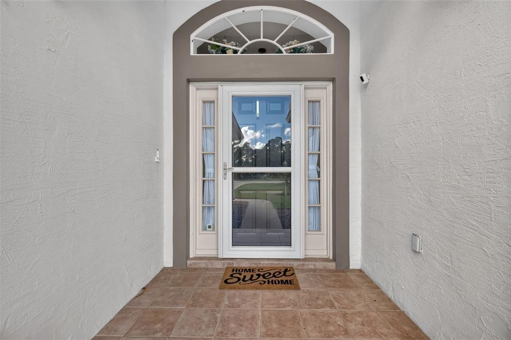 A front entryway features a glass storm door, sidelights, and a decorative arched transom window — 11506 LAKE DR, LEESBURG, FL