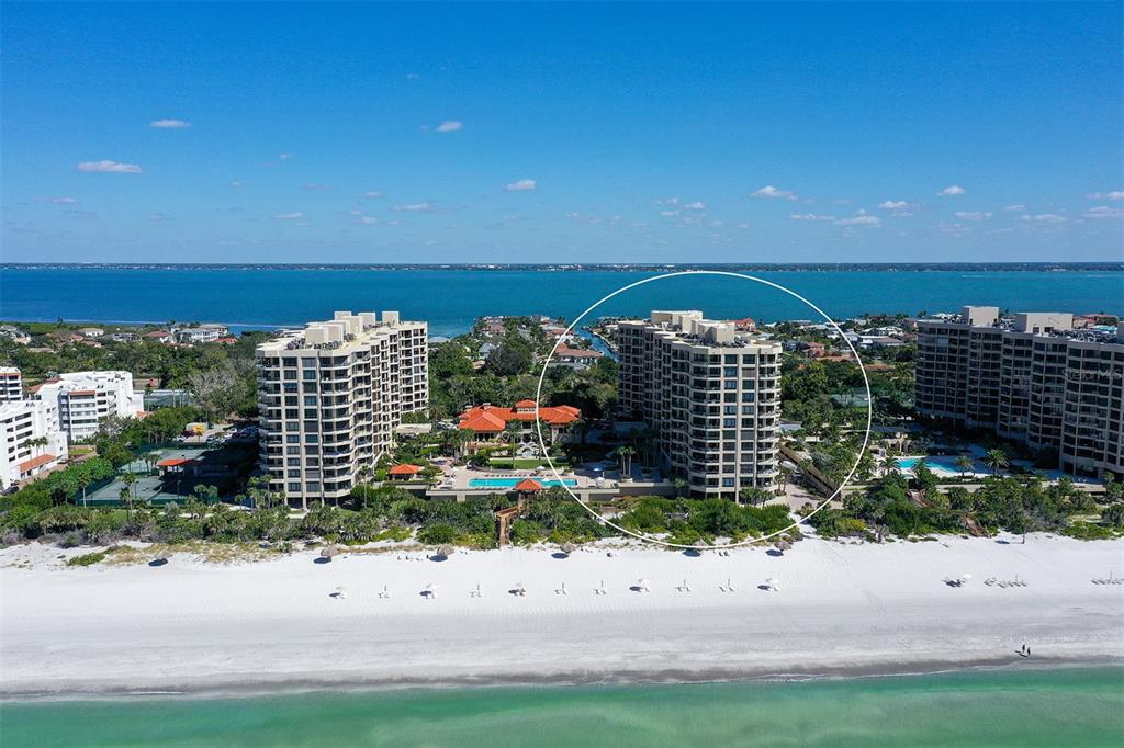 An aerial view shows a multi-story residential building circled on a sandy beach — 1241 GULF OF MEXICO DRIVE UNIT 303, LONGBOAT KEY, FL