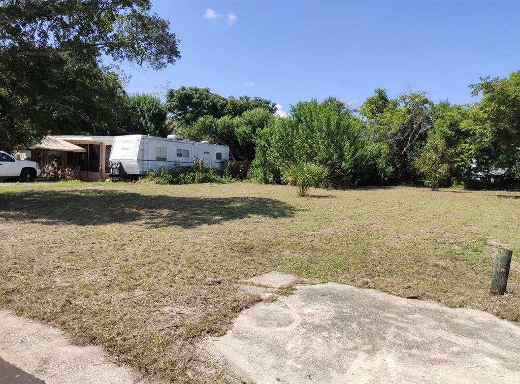 A grassy lot features a white travel trailer parked next to a small residential structure — 1403 DONNA, COCOA, FL