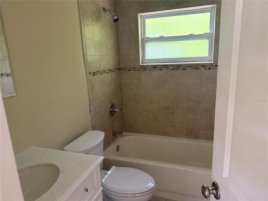 A bathroom features a vanity, a toilet, and a tiled shower-tub combination with a window — 7317 JANCZLIK DRIVE, NEW PORT RICHEY, FL