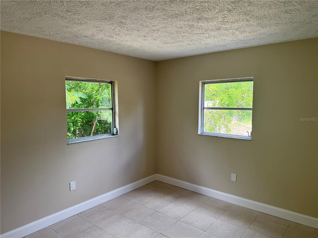 An empty room with beige walls, tile flooring, and two windows looking out at greenery — 7317 JANCZLIK DRIVE, NEW PORT RICHEY, FL