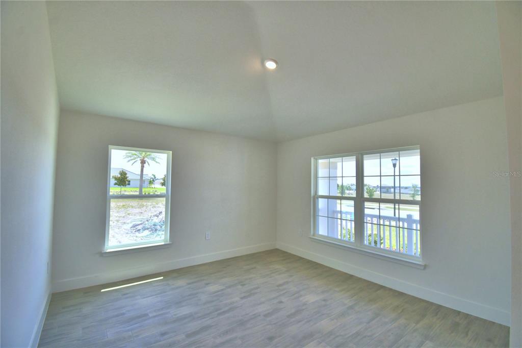 An empty room features light-colored wood-look flooring, white walls, and two windows with exterior views — 5415 WATERSIDE DRIVE, AUBURNDALE, FL