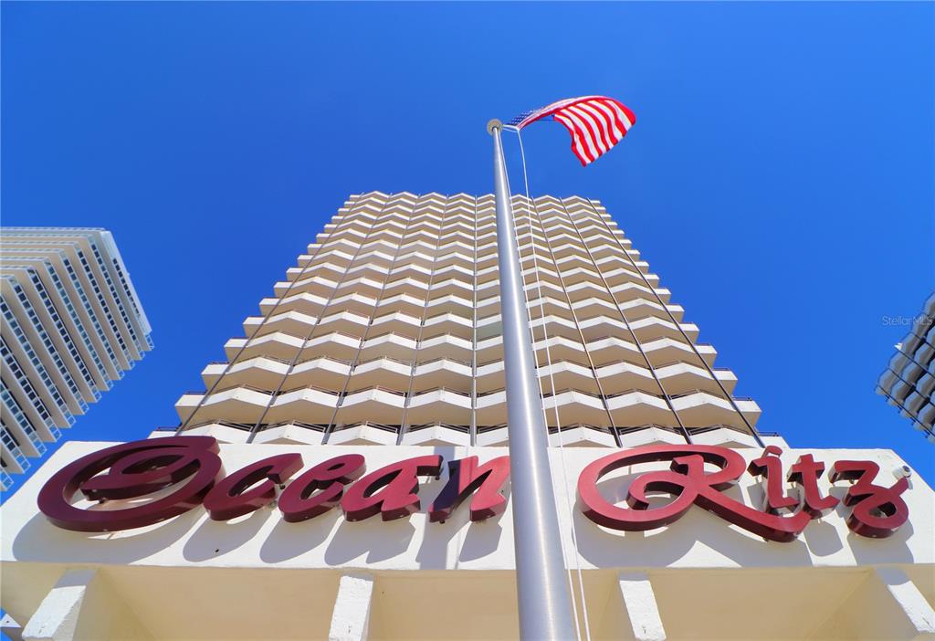 A low-angle exterior view of a high-rise building with a flag and signage — 2900 N ATLANTIC AVENUE UNIT 6060, DAYTONA BEACH, FL