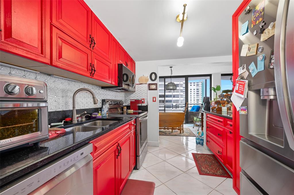 A kitchen features bright red cabinets, black countertops, stainless steel appliances, and a tiled floor — 2900 N ATLANTIC AVENUE UNIT 6060, DAYTONA BEACH, FL