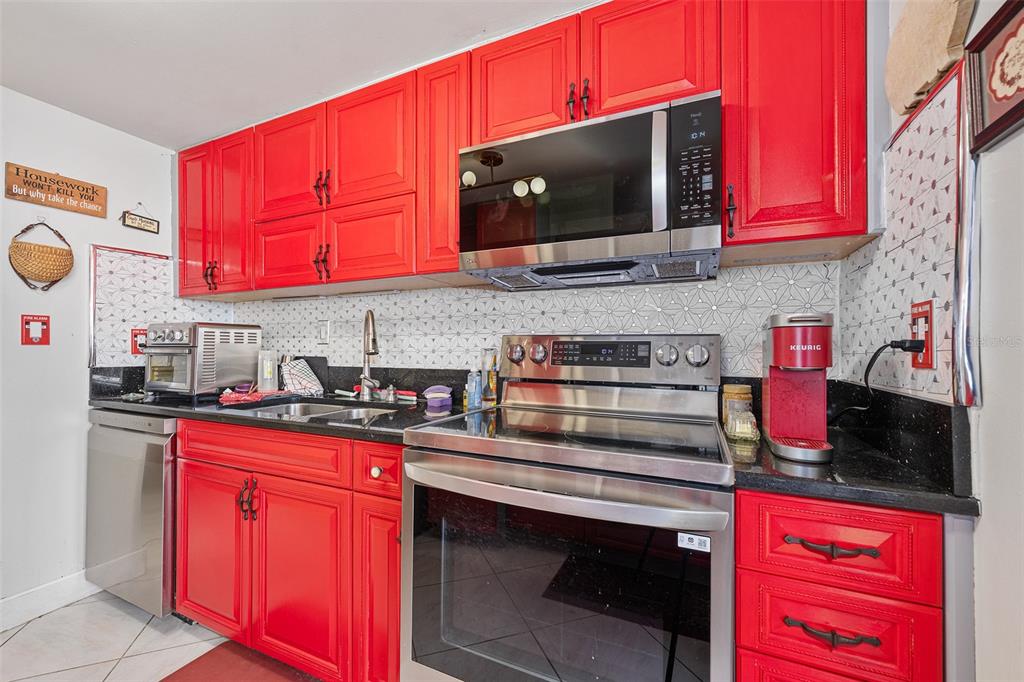 A kitchen features bright red cabinets, black countertops, stainless steel appliances, and patterned tile backsplash — 2900 N ATLANTIC AVENUE UNIT 6060, DAYTONA BEACH, FL