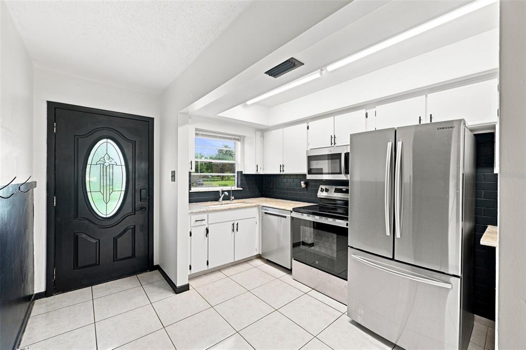 A kitchen features white cabinets, stainless steel appliances, a black tile backsplash, and a black door — 28850 LINDENHURST DRIVE, WESLEY CHAPEL, FL