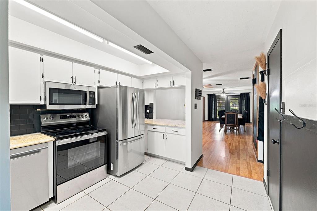 A kitchen with white cabinets, stainless steel appliances, and tile flooring opens to a dining area — 28850 LINDENHURST DRIVE, WESLEY CHAPEL, FL